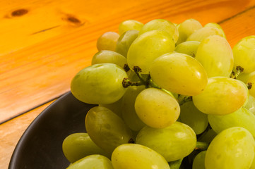 large brush of green grapes in a dark ceramic plate on a wooden background