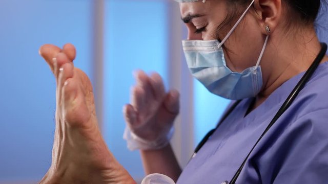 Funny Medical professional doctor nurse in (PPE) protective gloves, a face mask , a scrub cap, and a stethoscope  is repulsed by disgusting, dirty  bad odor produced by a patient's foot, because it st