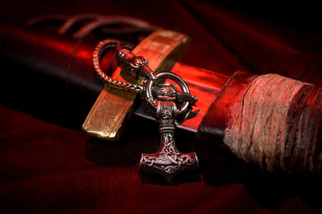 Viking battle sword made of steel with a leather handle with a Thor's silver Hammer pendant on a red black background. Handmade. Mjolnir. Viking's symbol