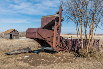 Fototapeta na wymiar Vintage pull-type combine and granary abandoned in a field in Saskatchewan, Canada