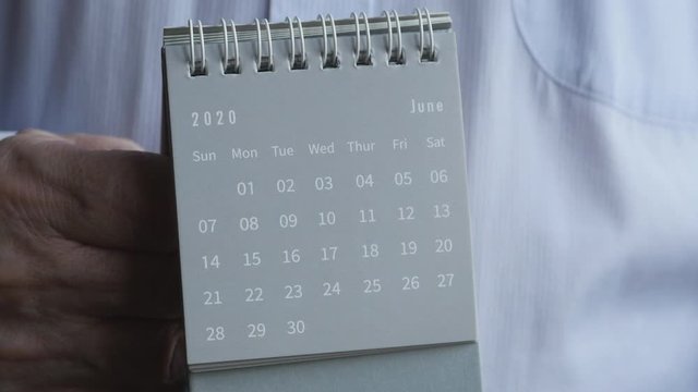 A Man's Hand Flips The Sheets Of A 2020 Year Black Mini Monthly Standing Desk Calendar From May To June Month.