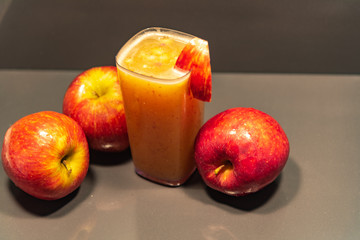 Glass of apple juice amid fruits on dark background