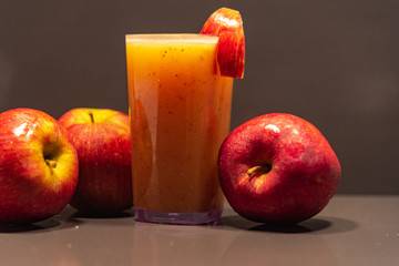 Glass of apple juice amid fruits on dark background