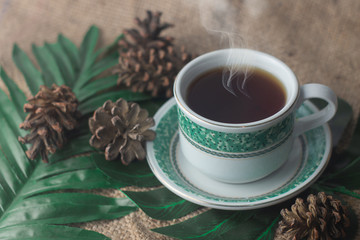Cup of black tea with smoke on burlap with leaves 