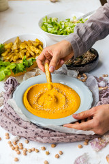Yellow chickpea hummus spread paste on plate in woman hands.