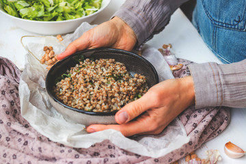 Russian traditional buckwheat porridge. Cooked grain with green spinach leaves in bowl. Woman hands hold vegan healthy food.