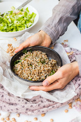 Russian traditional buckwheat porridge. Cooked grain with green spinach leaves in bowl. Woman hands hold vegan healthy food.