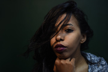 young african woman posing at studio, face with hand portrait over dark background	