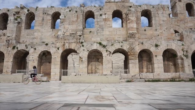 Odeon of Herodes Atticus, a girl on a bike passes in front of the marble stones