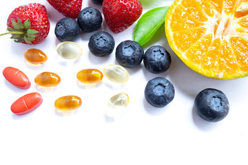 Vitamin supplement with healthy fruits blueberry, strawberry, and orange on white wood...