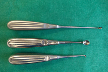 3 differently sized sharp spoons for an operation lie on a green surgical drape