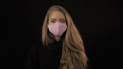 Young woman with golden hair pink medical mask. Isolated on black background. Health care and medical concept. Close up portrait . 4k. Coronavirus Epidemic, illness, pandemic