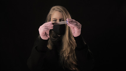 Girl in a black mask holds a test tube with blood and the inscription covid-19. Isolated on black background. Health care and medical concept. Coronavirus Epidemic