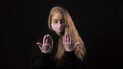 Girl in a pink mask and a ribbon with the inscription covid 19 rubs her palms. Isolated on black background. Health care and medical concept. Close up portrait . 4k. Coronavirus Epidemic