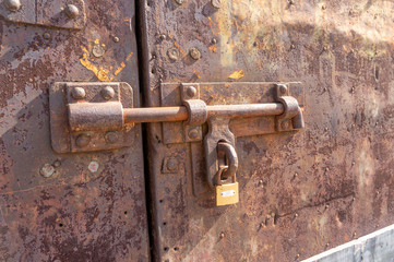 Old weathered bolt with lock on it and dated rusty factory gate in the background in the sunlight