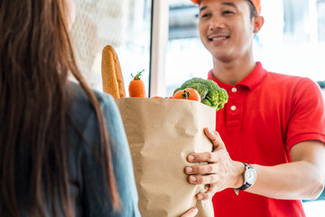 Asian deliver man worker in red color uniform handling bag of food, fruit, vegetable give to young...