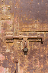 Old weathered bolt with lock on it and dated rusty factory gate in the background in the sunlight