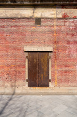 Old weathered rusty factory gate and the dated brown brick wall in the sunlight