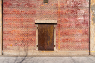 Old weathered rusty factory gate and the dated brown brick wall in the sunlight