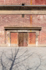 Old weathered rusty factory gate and the dated brown brick wall in the sunlight