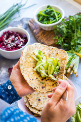 Woman hands filling plain flatbread tortilla with fresh vegetables salad to make a wrap at home kitchen.