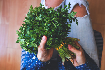 Woman holds a fresh green bunch of parsley at kitchen