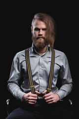 Portrait of a brutal stylish bearded man with a stylish haircut in a fashionable shirt with suspenders. Emotion of a smirk and a mysterious serious look.