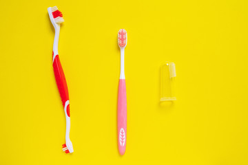 Different types of colored toothbrushes for people, dogs and pets isolated on yellow background. Daily oral hygiene on schedule for dental health. Double sided and transparent rubber finger brushes.