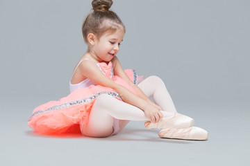 Cute charming ballerina little girl in pink tutu is sitting on the floor trying to put on ballet shoes © satyrenko