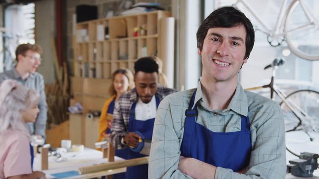 Portrait of male small business owner in workshop assembling hand built bamboo bicycles with staff working in background - shot in slow motion