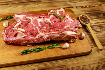 Raw fresh beef rib eye steak on bone with spices, garlic and rosemary on wooden table