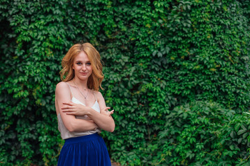 Naklejka premium Portrait of a young beautiful woman, standing next to the wall of wild grape leaves.