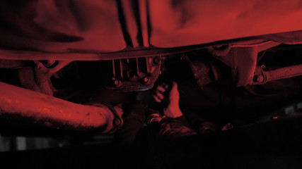 Fototapeta na wymiar Man hands screw bolts into gearbox cover in pit under machine