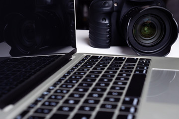 A black digital camera and a computer laptop on a table.