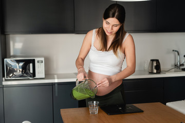 Young beautiful pregnant woman in expectation of a baby makes herself a tasty and healthy smoothie.