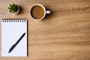 desk office with laptop, blank notepad, coffee cup and pen on wood table. Flat lay top view copy spce.