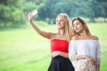 Beautiful girl with lovely friend resting or relaxing and selfie in a park, selfie picture by smart...