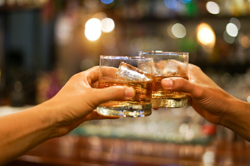 Two men clink glasses of whiskey drink alcoholic beverage together while at bar counter in the...