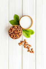 Almond milk near nuts on white wooden background top-down