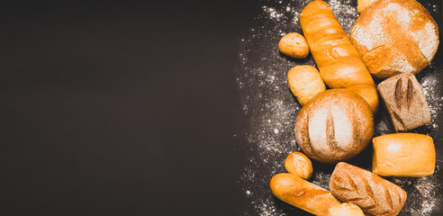 Assortment of fresh baked bread with a golden crust a black rustic background. Flat layout with place for advertisement.
