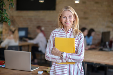 Blonde woman standing in the office, holding yellow folder