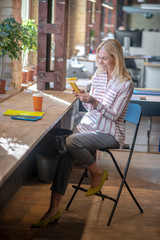 Blonde woman sitting on chair, checking her phone, smiling