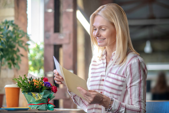 Happy blonde woman received letter and flowers, smiling