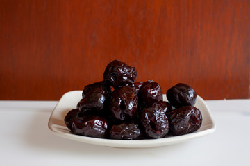 Red Dates, also known as jujube on white plate with wooden background