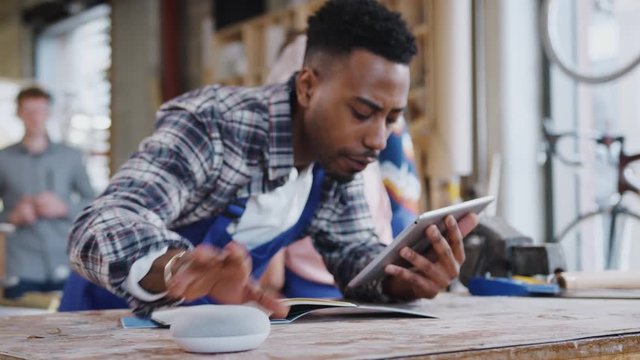 Focus pulls from background to foreground as male worker in carpentry workshop uses digital tablet and asks smart speaker question - shot in slow motion