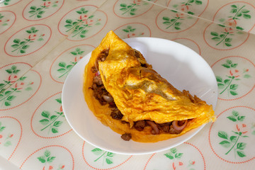 Omelette, a delicious homemade omelet with meat and onion served on a white plate on the table.