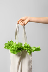 Female hand with fresh lettuce in eco bag on color background