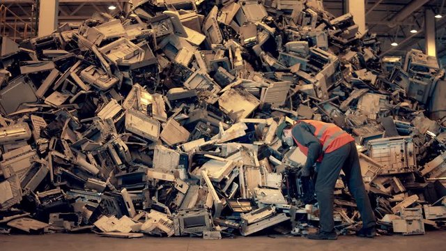 Electronic garbage recycling factory. Landfill inspector is throwing waste debris into a pile