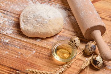 Dough with oil, eggs and rolling pin on wooden background