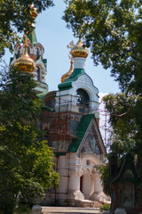 Fototapeta na wymiar Golden domes, restoration of the temple view through the foliage